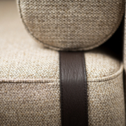 Gros plan d'un canapé texturé beige avec un détail de sangle en cuir foncé, présentant une qualité exceptionnelle qui en fait une pièce remarquable dans n'importe quelle salle d'exposition. Canape Paris by Atelier Bis