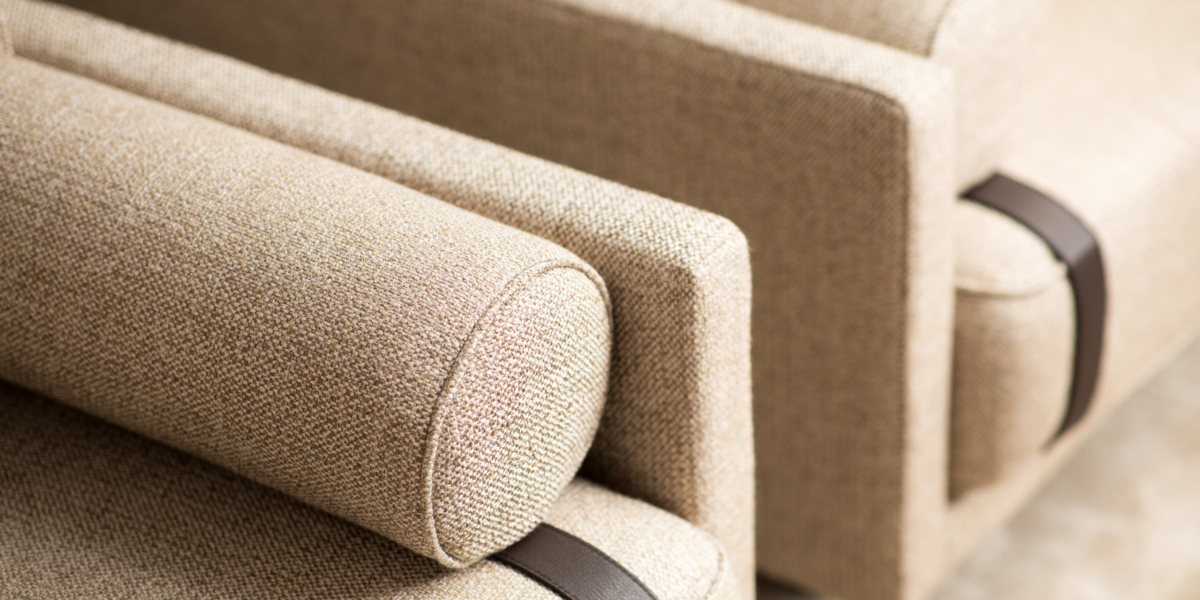 Gros plan de deux fauteuils en tissu beige avec coussins cylindriques et sangles marron foncé sur les accoudoirs, dégageant un charme parisien rappelant un canapé lounge chic. Canape Paris by Atelier Bis