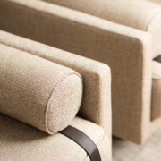 Gros plan de deux fauteuils en tissu beige avec coussins cylindriques et sangles marron foncé sur les accoudoirs, dégageant un charme parisien rappelant un canapé lounge chic. Canape Paris by Atelier Bis