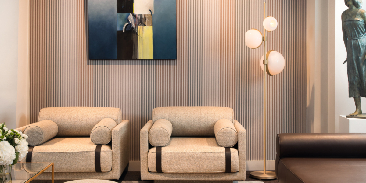 Un salon parisien moderne avec des sièges beiges, de l'art abstrait et un lustre circulaire, avec une sculpture élégamment positionnée sur la droite. Canape Paris by Atelier Bis