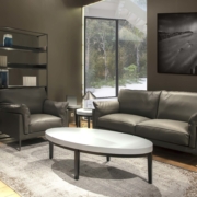 Salon moderne comprenant un canapé et un fauteuil gris, une table basse ovale, des étagères élégantes et une grande fenêtre qui respire la qualité parisienne. Canape Paris by Atelier Bis