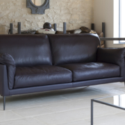 Un canapé en cuir noir de haute qualité orne le salon moderne, accentuant les murs en pierre et la décoration minimaliste - c'est une pièce maîtresse époustouflante qui pourrait facilement être la star de n'importe quelle salle d'exposition. Canape Paris by Atelier Bis