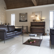 Un salon moderne est doté de deux canapés noirs rappelant l'élégance d'une salle d'exposition, complétés par une élégante table basse en verre et un piano. Le mur d'accent en pierre ajoute une touche de qualité, rendant cet espace à la fois élégant et accueillant. Canape Paris by Atelier Bis