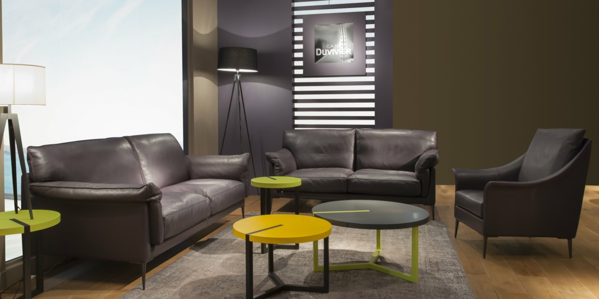 Salon moderne avec des canapés sombres, des tables jaunes et vertes, un lampadaire et des œuvres d'art encadrées sur le mur, dégageant une touche de qualité parisienne. Canape Paris by Atelier Bis