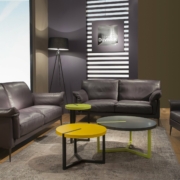 Salon moderne avec des canapés sombres, des tables jaunes et vertes, un lampadaire et des œuvres d'art encadrées sur le mur, dégageant une touche de qualité parisienne. Canape Paris by Atelier Bis