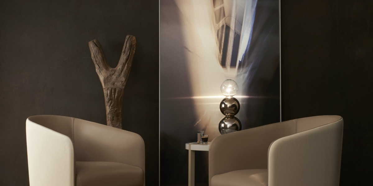 Deux chaises beiges se font face dans une salle d'exposition aux murs sombres, avec des œuvres d'art exquises, une sculpture en bois et une petite table ornée de décorations. Canape Paris by Atelier Bis