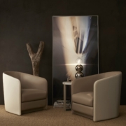 Deux chaises beiges se font face dans une salle d'exposition aux murs sombres, avec des œuvres d'art exquises, une sculpture en bois et une petite table ornée de décorations. Canape Paris by Atelier Bis