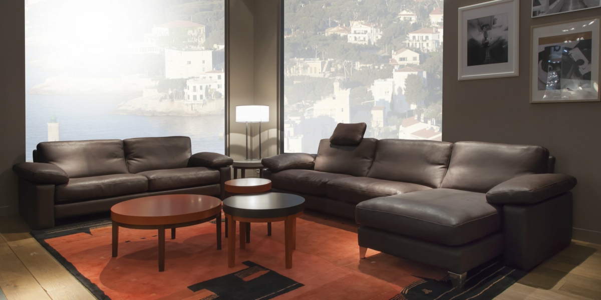 Salon confortable avec des canapés en cuir marron rappelant l'élégance d'un showroom parisien, des tables basses rondes et des œuvres d'art murales près d'une grande fenêtre avec une vue panoramique. Canape Paris by Atelier Bis