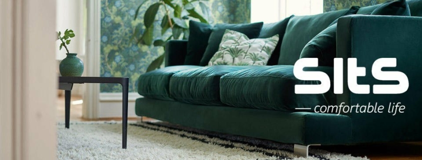 Un canapé vert avec des coussins fleuris dans un salon avec du papier peint vert et une plante luxuriante. Découvrez l'élégance parisienne avec une qualité inégalée, en ajoutant une touche de confort sophistiqué à votre vie à un prix exceptionnel. Une vie confortable. Canape Paris by Atelier Bis