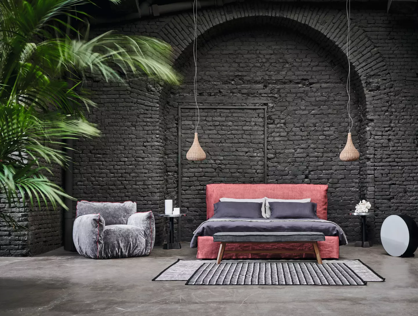 Découvrez une chambre moderne qui ressemble à une salle d'exposition élégante, avec des murs en briques sombres, un lit rose, des lumières suspendues, un fauteuil gris et des plantes vertes vibrantes - chaque élément se mélangeant parfaitement pour refléter une qualité exceptionnelle. Canape Paris by Atelier Bis