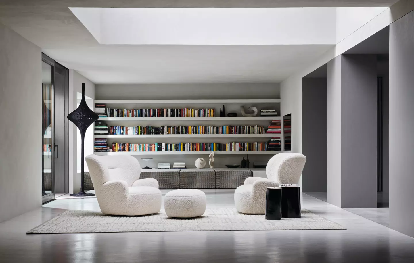 Salon moderne avec deux fauteuils blancs, un canapé cosy, un pouf et des étagères, le tout joliment disposé sous une lucarne. Canape Paris by Atelier Bis