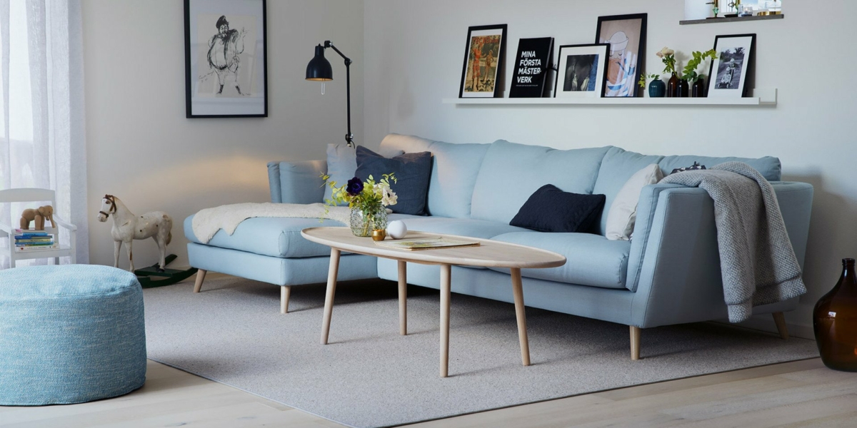 Salon cosy avec un canapé bleu clair, une table ronde en bois, une décoration murale rappelant Paris et un lampadaire. Canape Paris by Atelier Bis