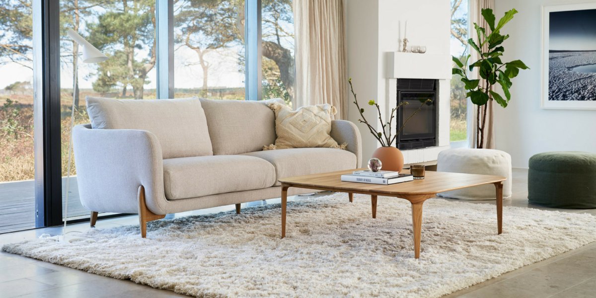 Un salon confortable doté d'un canapé beige de haute qualité, d'une table basse en bois et d'un tapis moelleux, le tout face à de grandes fenêtres offrant une vue imprenable sur le jardin. Canape Paris by Atelier Bis