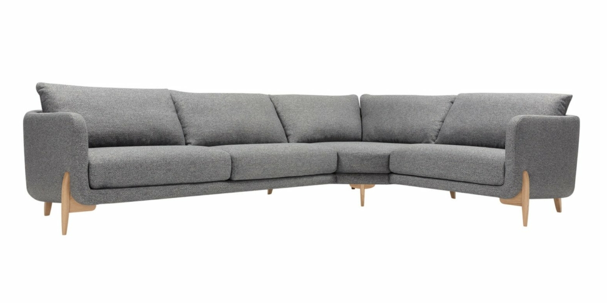 Canapé gris en L avec pieds en bois et coussins moelleux, présenté dans une salle d'exposition, vu sous un angle légèrement surélevé. Canape Paris by Atelier Bis