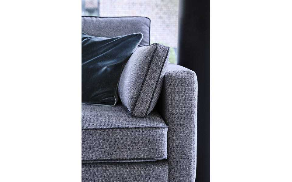 canape-4-places-peter-200-cm-4 Gros plan d'un canapé gris rembourré avec un coussin moelleux vert foncé dans une salle d'exposition chic, devant une fenêtre en arrière-plan. Canape Paris by Atelier Bis