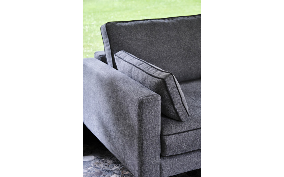 canape-4-places-peter-200-cm-5 Canapé en tissu gris avec un coussin assorti, élégamment placé devant une fenêtre offrant une vue verdoyante, rappelant un showroom parisien. Canape Paris by Atelier Bis