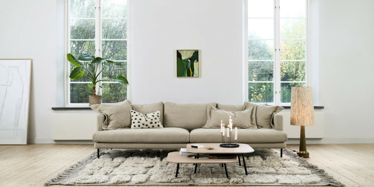 6_BRITT_interior_4seater_heather_2_-light_beige_1 Un salon avec un canapé modulable beige, des coussins colorés et un éclairage chaleureux.