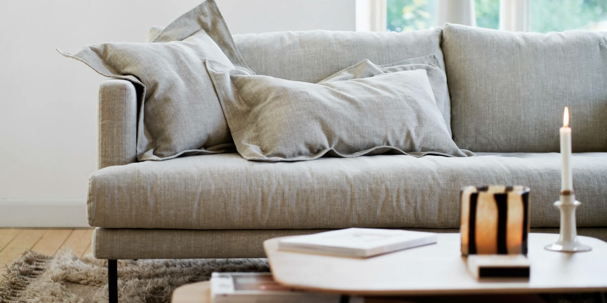 61cedbe303a8ee9bd6ac140b_2_BRITT_interior_set2_caleido_stampato_1_natur_3 Une pièce avec des meubles scandinaves, un tapis à motifs géométriques et des plantes suspendues.