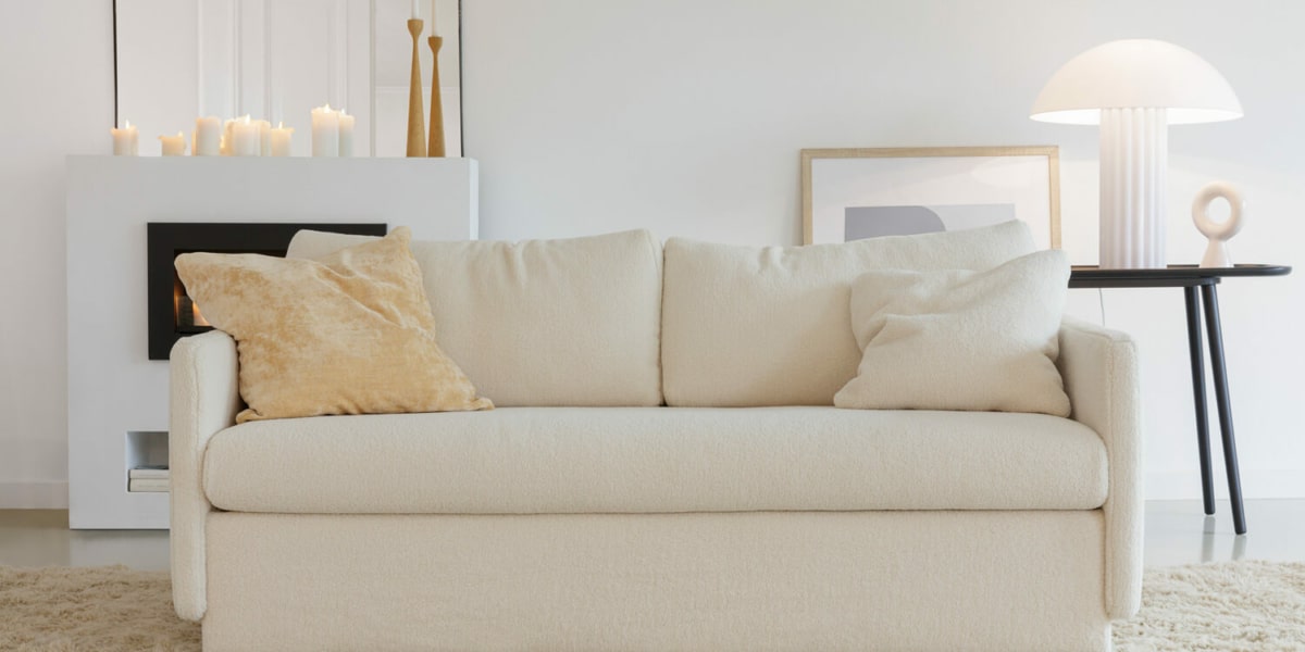 Canapé convertible en lit Colin en blanc avec des coussins beige assortis Le canapé Colin en blanc est accompagné de coussins beige assortis, créant une ambiance élégante et apaisante dans le salon.