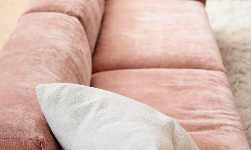 61cedca1ec15b58ca4ecaa73_EDDA_interior_set1_wildflower_8_dust_pink_5 Un espace décoré avec un canapé modulable rose, une table basse en verre et des œuvres d'art abstraites.