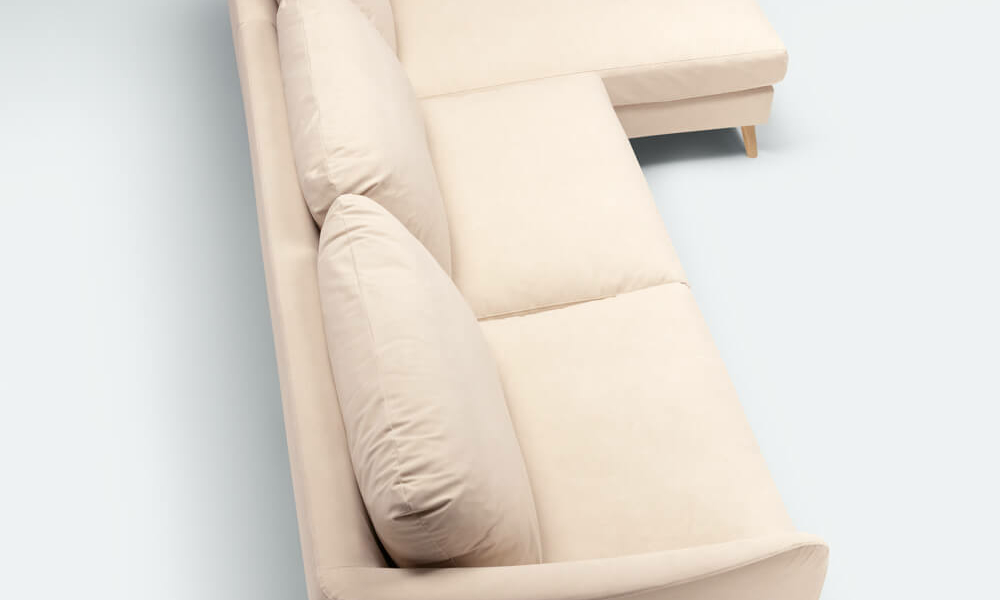 Canapé sectionnel en L beige avec pieds en bois présenté dans un showroom parisien sur fond gris clair. Canape Paris by Atelier Bis