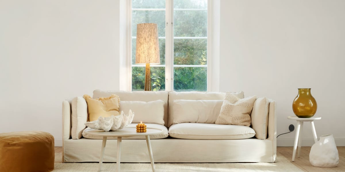 61cedf3215d4245e34c1e775_1_VIDAR_3,5seater_timber_6_cream_FATTY_footstool_classic_velvet_21_ caramel_1 Canapé Vidar blanc près d'une grande fenêtre avec vue sur la ville Placé près d'une grande fenêtre, le canapé offre une vue imprenable sur la ville. La lumière naturelle inonde la pièce, créant une atmosphère chaleureuse et accueillante.