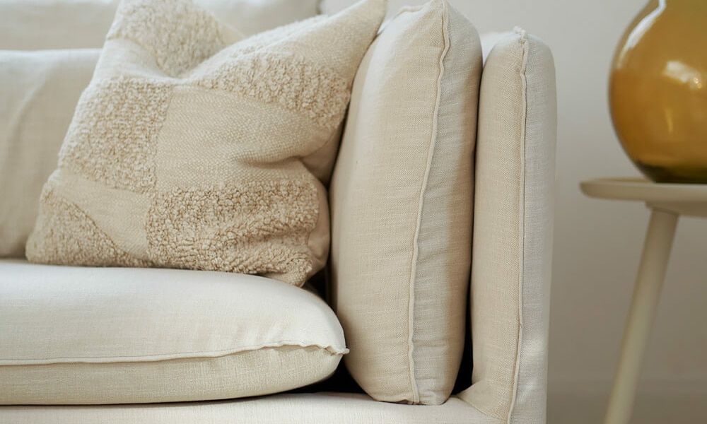 61cedf33d0a0a55591ecba97_2_VIDAR_3,5seater_timber_6_cream_2 Canapé Vidar marron dans un salon avec des murs beige clair et un tapis assorti Le canapé se trouve dans un salon aux murs beige clair, harmonisé avec un tapis assorti. La lumière naturelle illumine l'espace, mettant en valeur les tons chauds et les textures confortables.