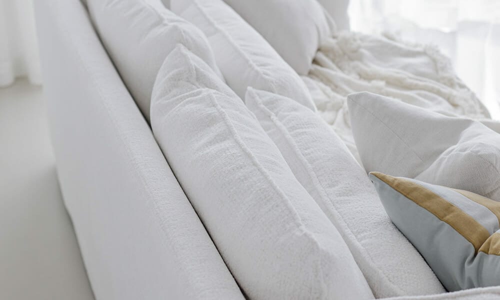 61cedf3c62c168ea3a6f27c7_5_VIDAR_interior_3,5seater_sky_1_off-white_3 Canapé Vidar blanc avec des coussins bleus et une table basse en marbre Le canapé est agrémenté de coussins bleus qui ajoutent une touche de couleur. Une table basse en marbre se trouve devant, apportant une note élégante et raffinée au salon lumineux.