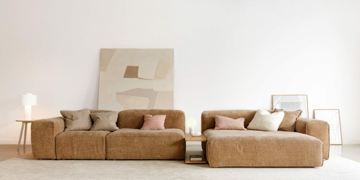 61f964362f71edebb5a3b5e4_1_EDDA Un espace décoré avec un canapé modulable bleu, une table basse en verre et des œuvres d'art abstraites.