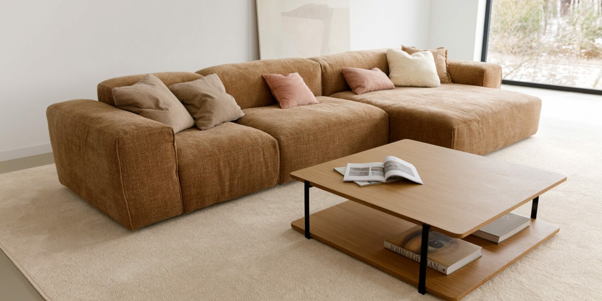 61f964416db2a043edfa789c_5_EDDA Une pièce avec un canapé en velours gris, des rideaux assortis et un tapis à motifs géométriques.