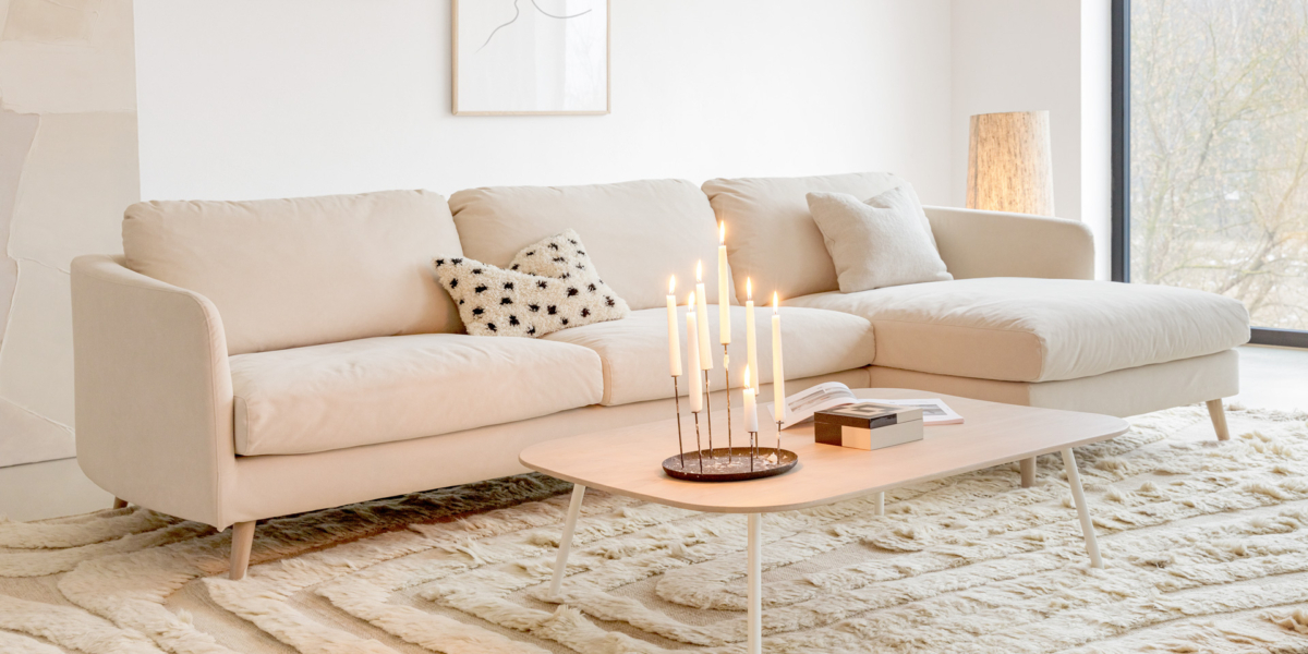 Salon minimaliste comprenant un canapé crème, un oreiller à motifs, une table basse éclairée aux bougies, de l'art abstrait et une grande fenêtre. Canape Paris by Atelier Bis