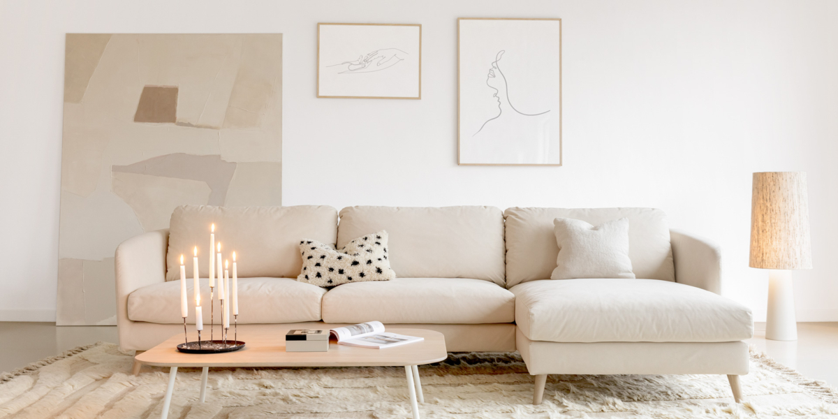 Un salon moderne avec un canapé d'angle beige, des œuvres d'art abstraites et une table basse en bois : on se croirait dans un showroom parisien. Une composition de bougies allumées ajoute une touche de qualité et de sophistication. Canape Paris by Atelier Bis