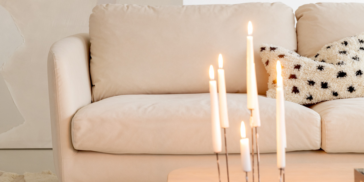 Un salon minimaliste à Paris présente un canapé beige, un tapis texturé et des bougies allumées sur une table basse en bois, créant une ambiance digne d'un showroom chic. Canape Paris by Atelier Bis