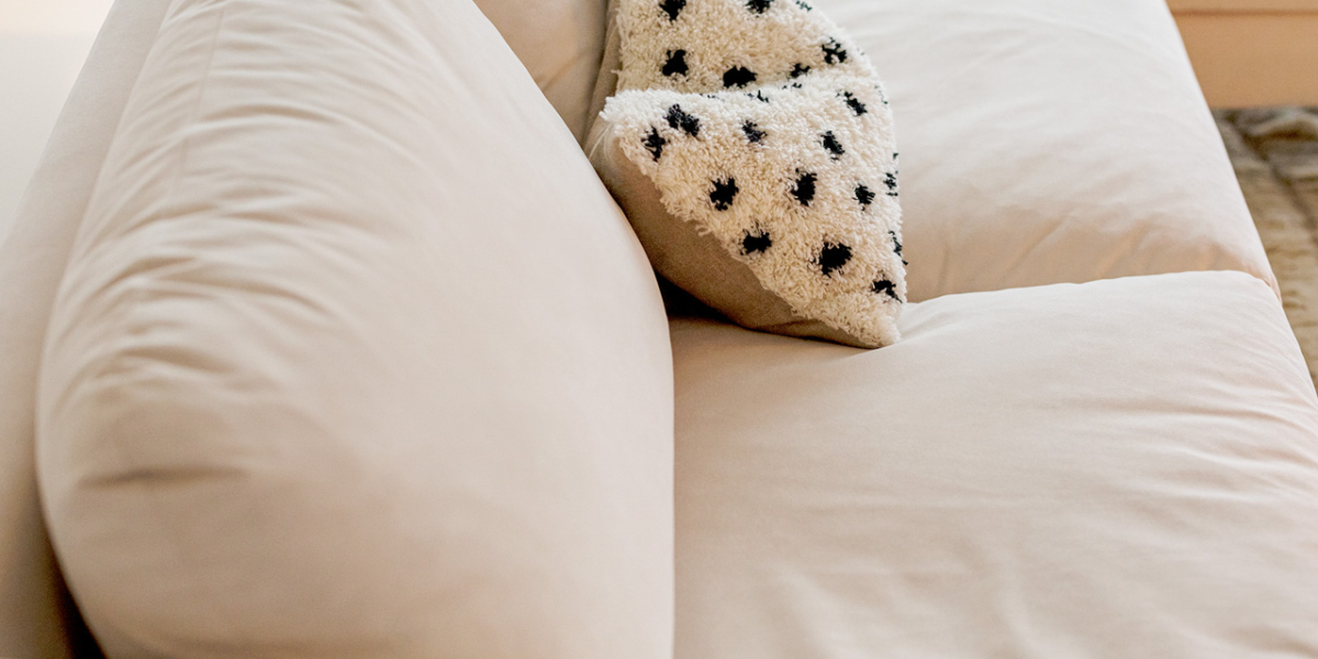 Dans un charmant showroom parisien, un canapé sectionnel beige présente un coussin à motif étoilé, parfaitement complété par la lampe à la lumière chaleureuse à côté de la fenêtre. Canape Paris by Atelier Bis