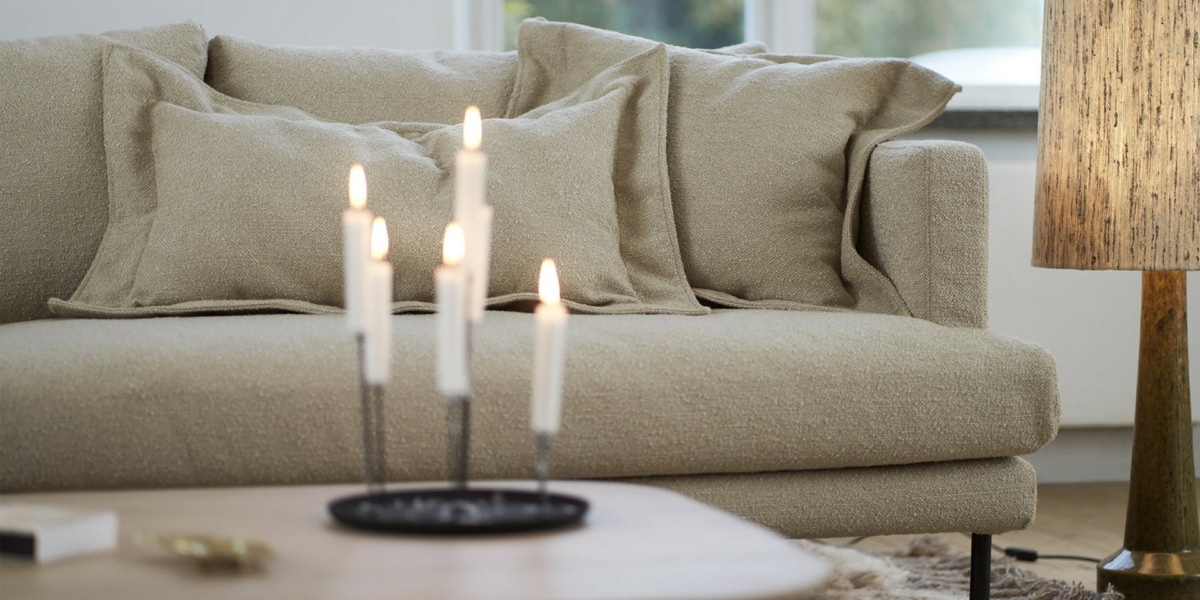 7_BRITT_interior_4seater_heather_2_-light_beige_3 Un espace industriel avec un canapé en cuir noir, des murs en briques apparentes et des étagères métalliques.