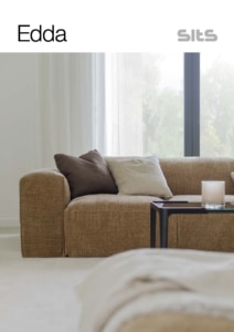 edda-0-pdf Salon cosy avec un canapé marron, des coussins et une table basse avec une bougie près d'une grande vitrine de style showroom qui ajoute une lumière de qualité, évoquant le charme de Paris. Canape Paris by Atelier Bis