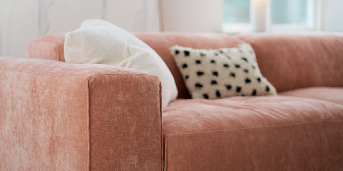 EDDA_interior_set1_wildflower_8_dust_pink_4 Un salon scandinave avec un canapé rose clair, des coussins en lin et un tapis en jute.