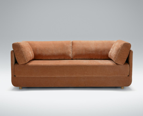 Un canapé en velours marron avec deux coussins sur un fond gris clair respire la qualité parisienne. Canape Paris by Atelier Bis