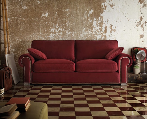 Un charmant canapé orné de coussins repose contre un mur vieilli, posé sur un sol à carreaux avec des objets de décoration éparpillés, prêt à voler la vedette dans n'importe quelle salle d'exposition. Canape Paris by Atelier Bis