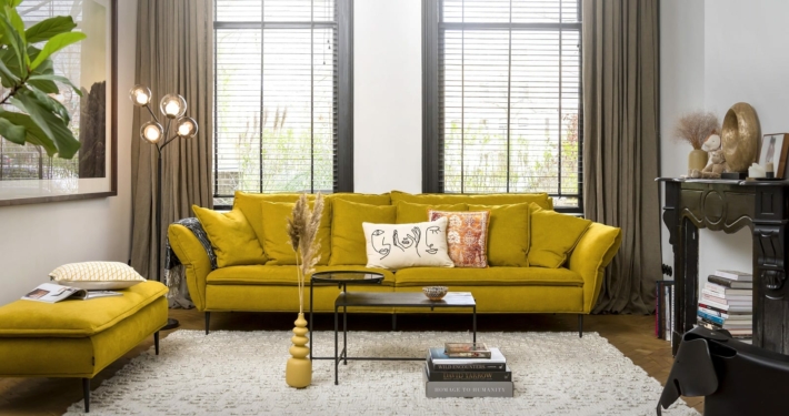 Salon avec un canapé jaune, un pouf assorti, des accents abstraits, un grand tapis, de hautes lampes et des œuvres d'art encadrées au mur : une vitrine qui pourrait orner n'importe quel showroom parisien. Canape Paris by Atelier Bis