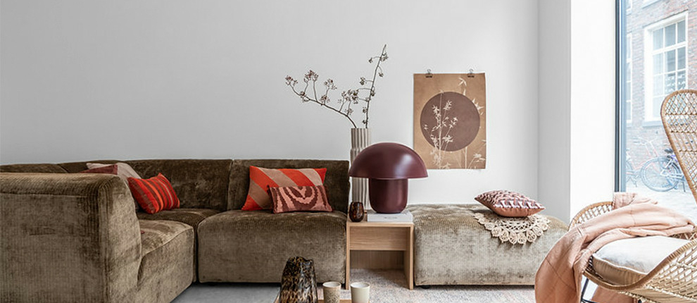 Salon cosy avec un canapé sectionnel marron de haute qualité, des coussins décoratifs, une petite table en bois et une chaise en osier près de la fenêtre, évoquant le charme du style parisien. Canape Paris by Atelier Bis