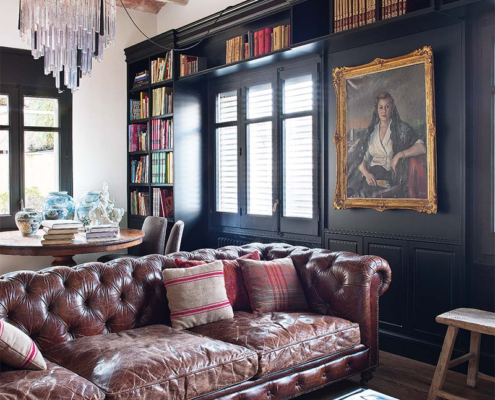 Découvrez un salon chaleureux arborant un luxueux canapé en cuir marron, entouré d'élégantes bibliothèques et illuminé par un superbe lustre. L'espace respire la sophistication avec ses œuvres d'art et son plafond en bois orné d'accents de brique, créant un showroom d'une qualité intemporelle. Canape Paris by Atelier Bis